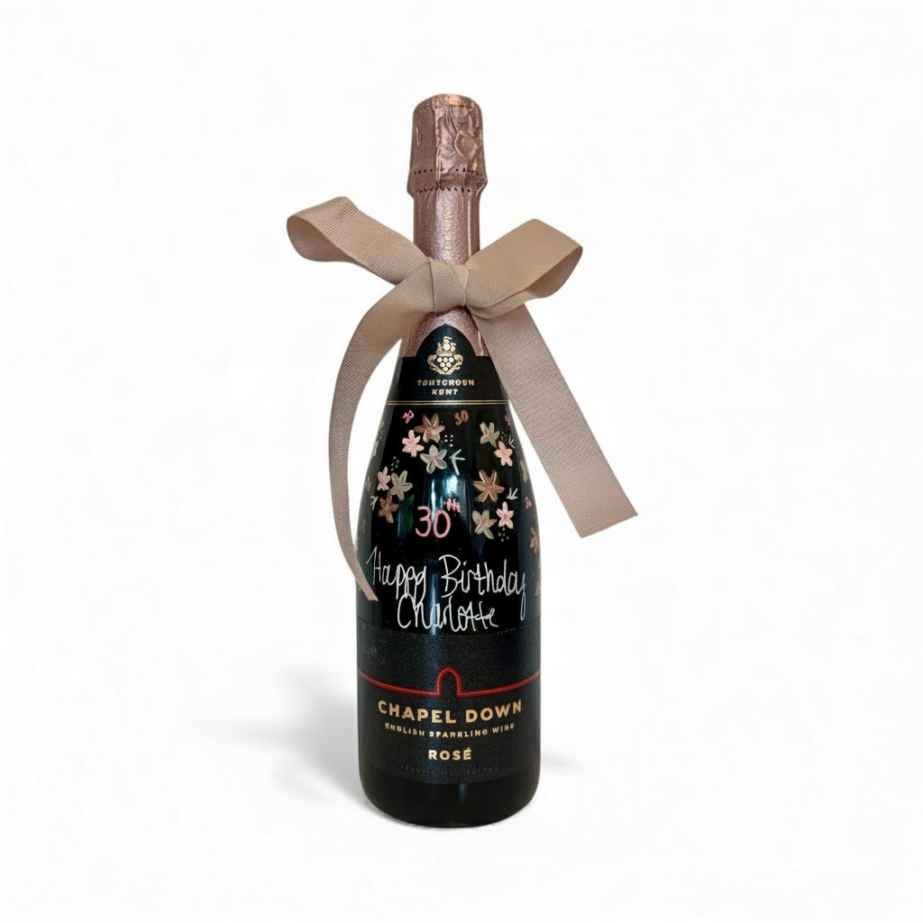 Bottle of Chapel Down Rosé champagne with decorative bow and personalized text on a white background